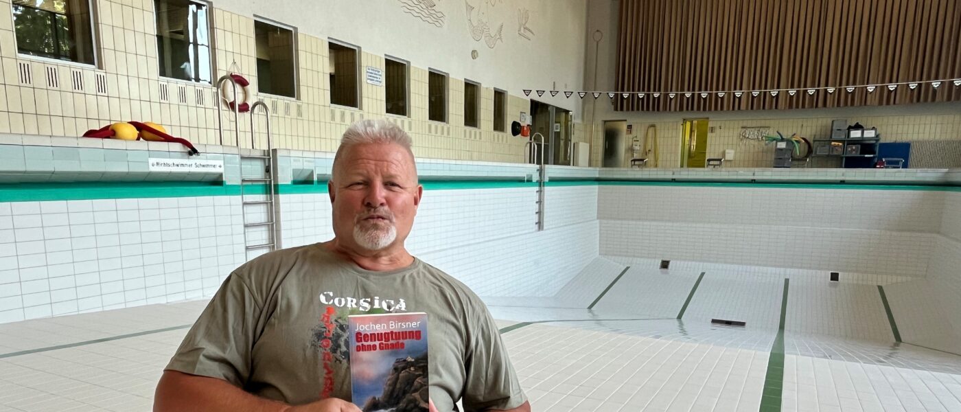 Ein Mann hält ein Buch in die Kamera, während er in einem leeren Schwimmbecken sitzt