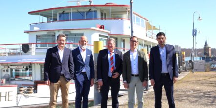 Fünf Männer in Anzügen stehen vor einem weißen Schiff