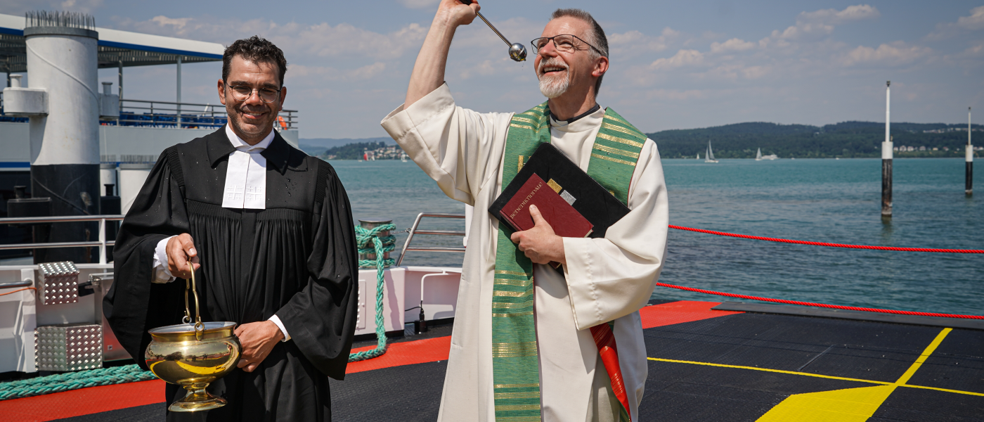 Ein evangelischer und ein katholischer Pfarrer segnen das neue Fährschiff Richmond bei der Taufe mit Weihwasser.