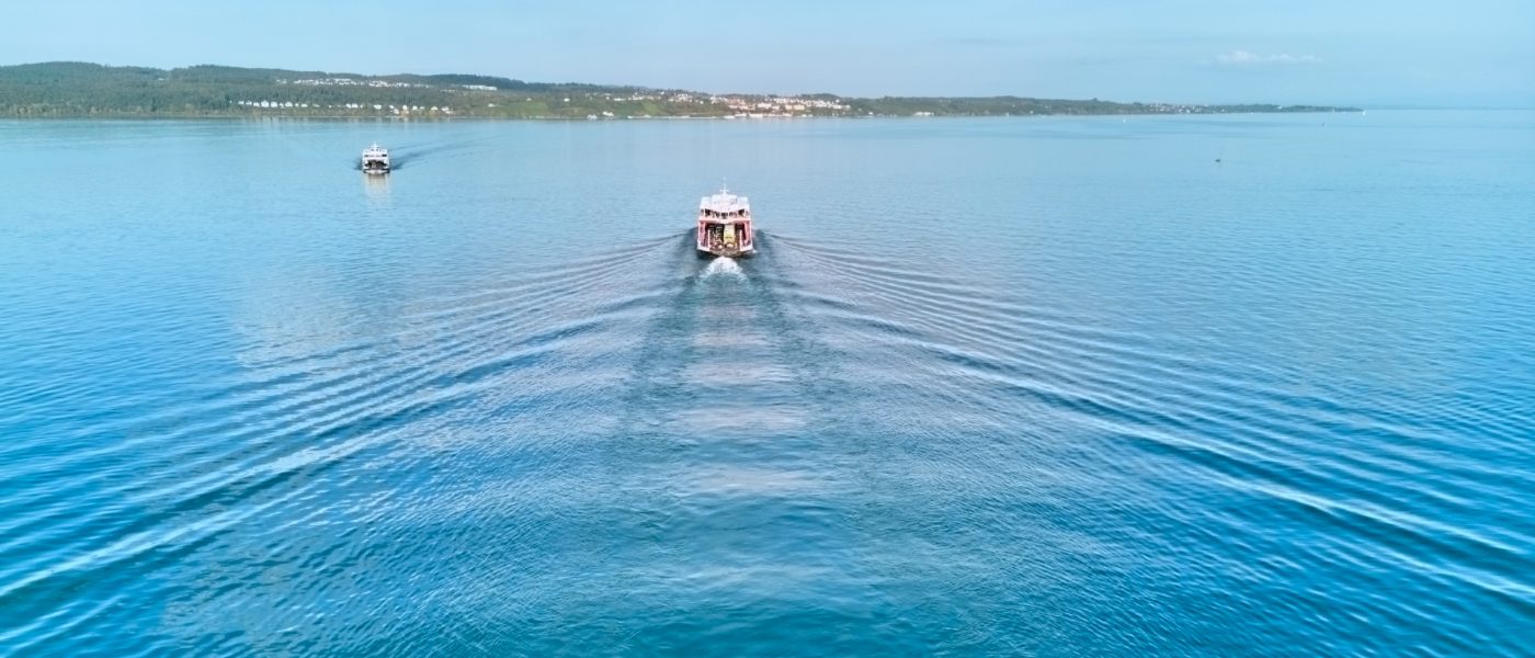 Zwei Fähren kreuzen sich auf dem Wasser, im Hintergrund sieht man Meersburg.